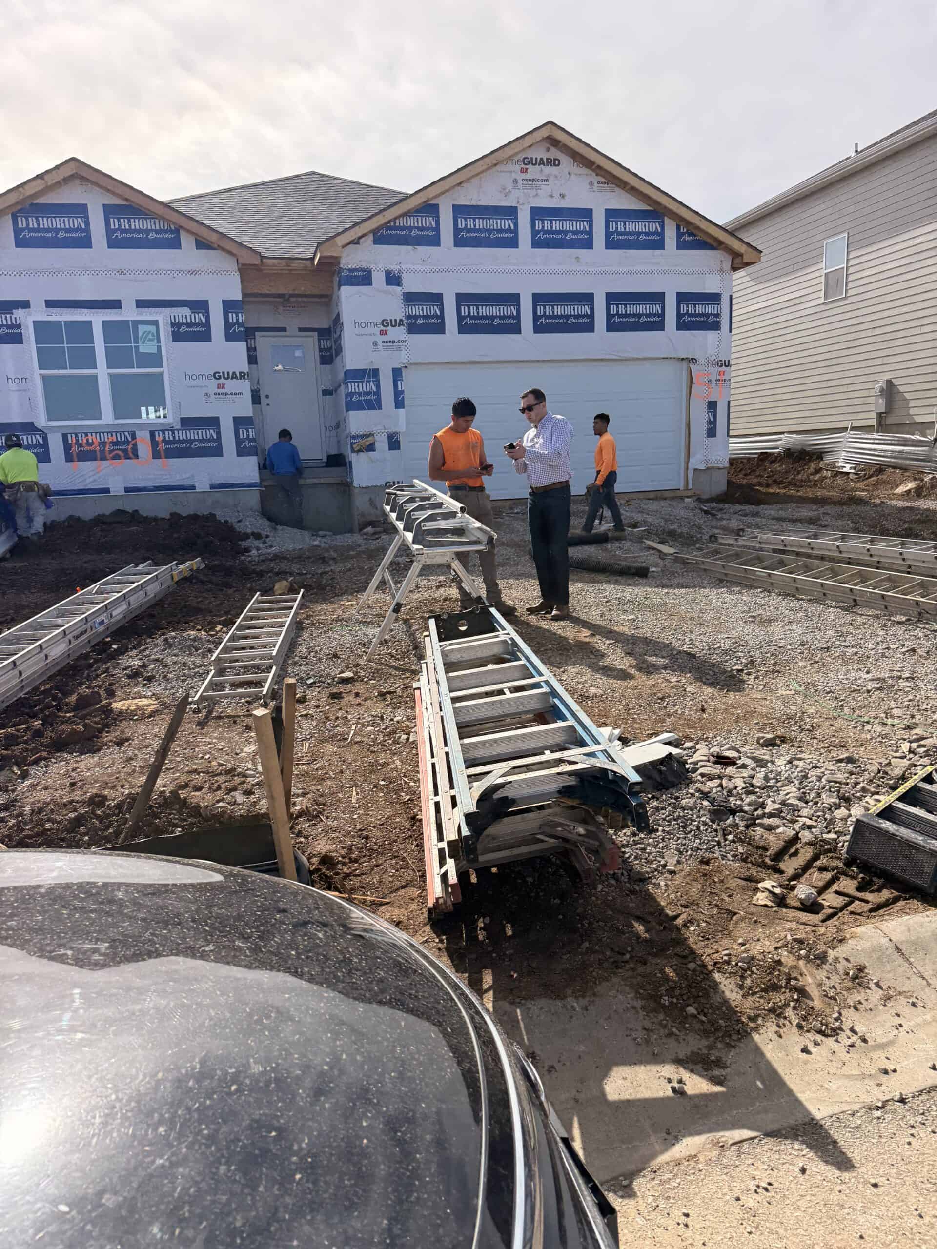 Stag Homes team members reviewing plans on-site during a home addition project in Kansas City, with framing underway and construction materials staged in front of a newly built residential structure.