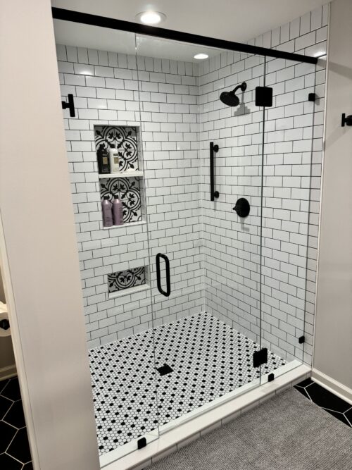 Glass-enclosed shower Glass-enclosed shower with white subway tiles, black fixtures, and patterned tile accent inset